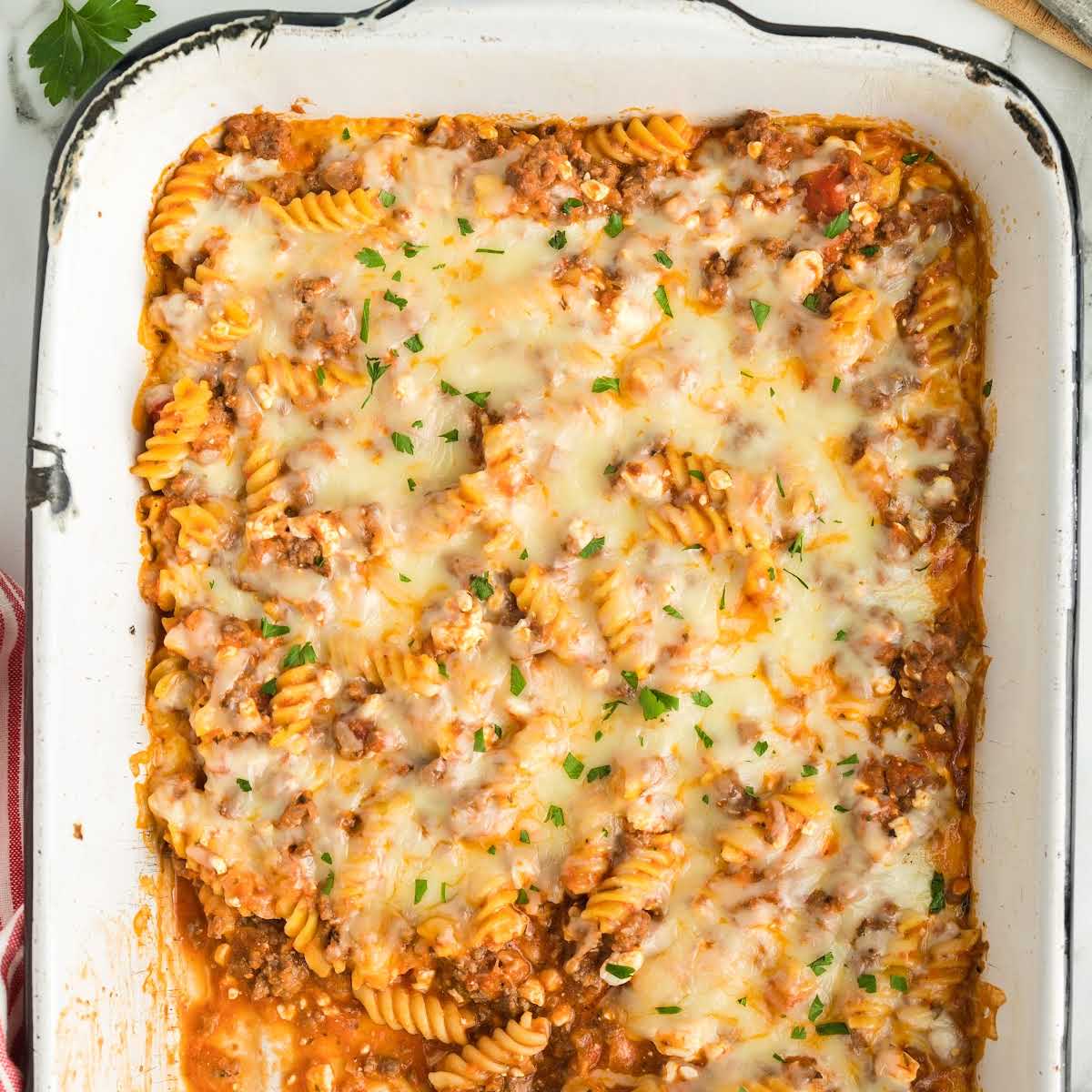 Overhead shot of a partially served lasagna casserole, with a spoonful being lifted from a cheesy, saucy center.
