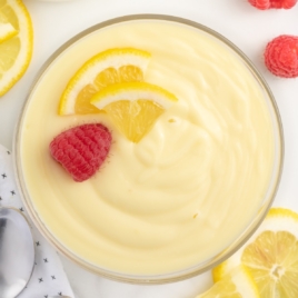 Creamy bowl of lemon custard with a fresh slice of lemon and a fresh raspberry