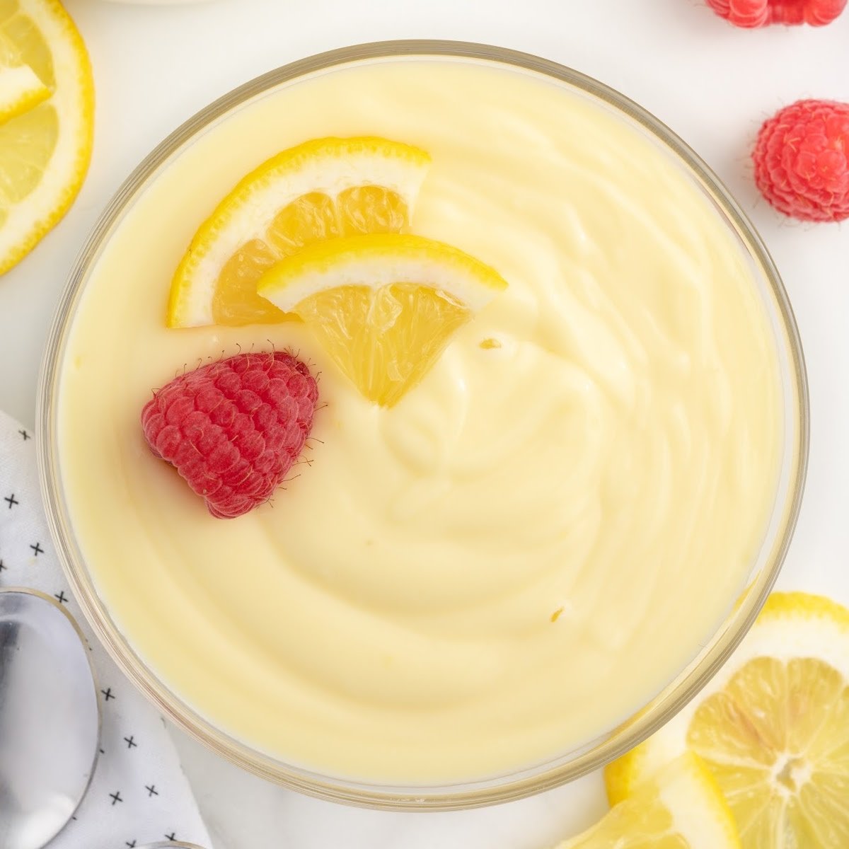 Creamy bowl of lemon custard with a fresh slice of lemon and a fresh raspberry