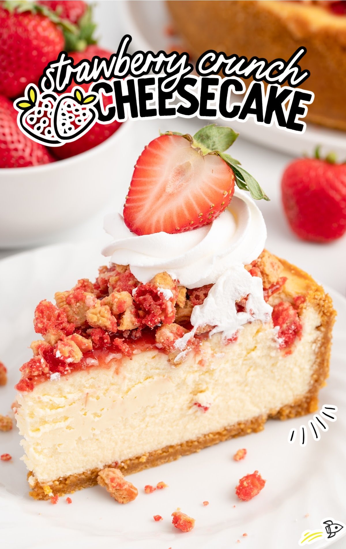 slice of strawberry crunch cheesecake on a plate topped with whipped cream and a fresh sliced strawberry