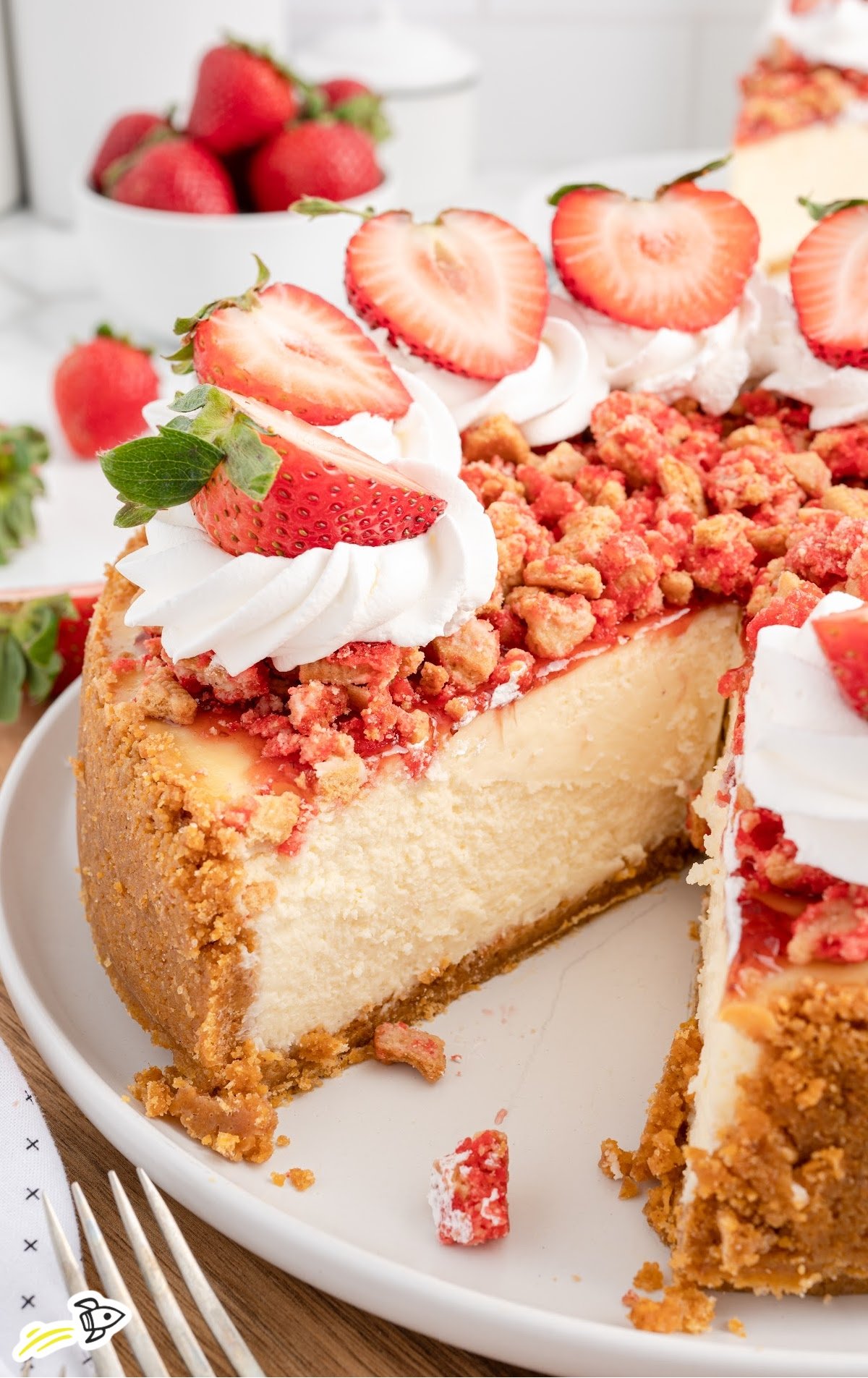 sliced strawberry crunch cheesecake with whipped cream and fresh berries