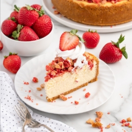 slice of strawberry crunch cheesecake on a plate topped with whipped cream and fresh strawberries