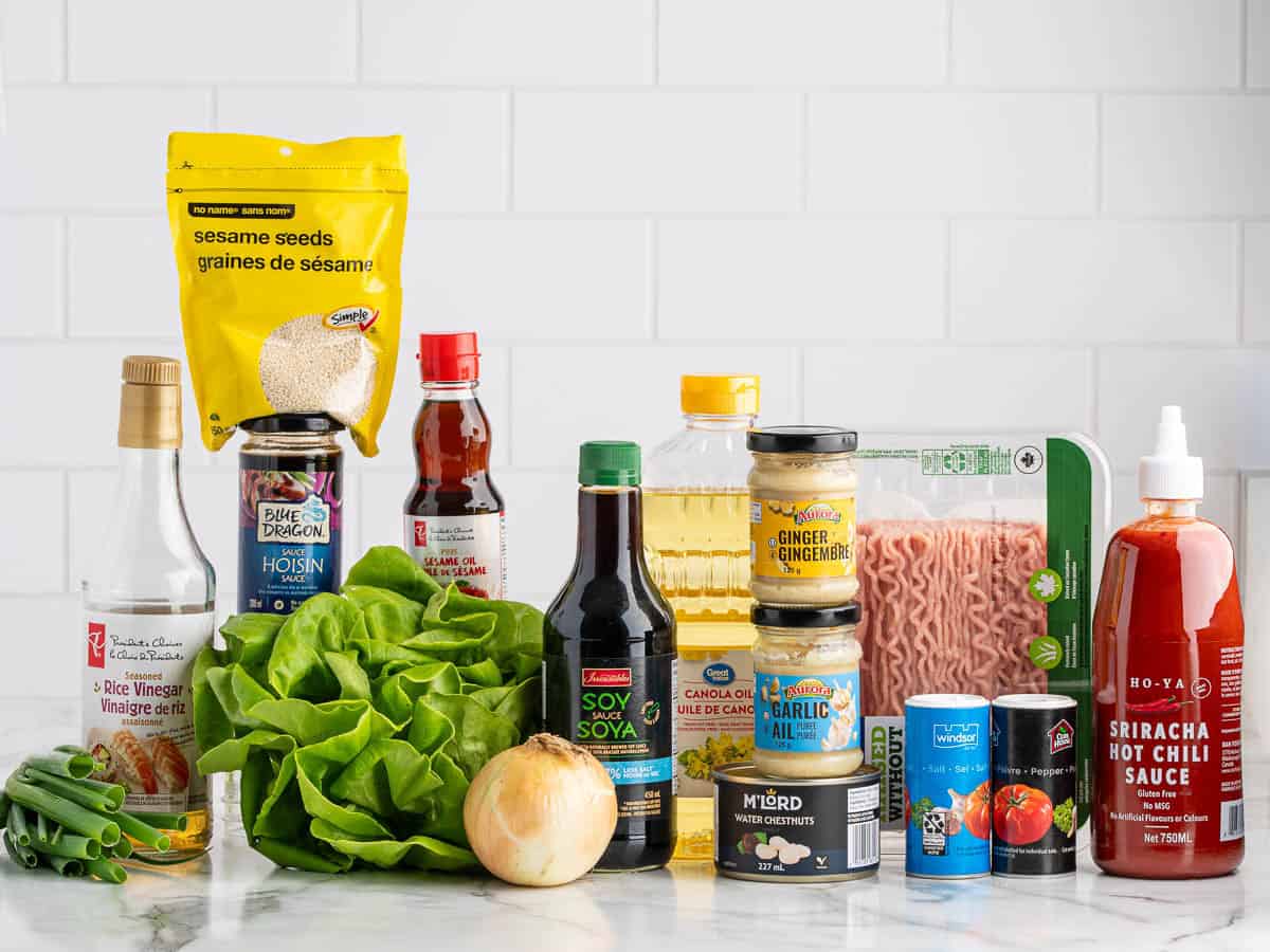 An assortment of ingredients on a counter, including lettuce, soy sauce, ground meat, onion, green onions, sesame seeds, hot chili sauce, oil, rice vinegar, canned water chestnuts, and ginger garlic paste—perfect for creating a delicious Asian Chicken Lettuce Wrap Recipe at home.
