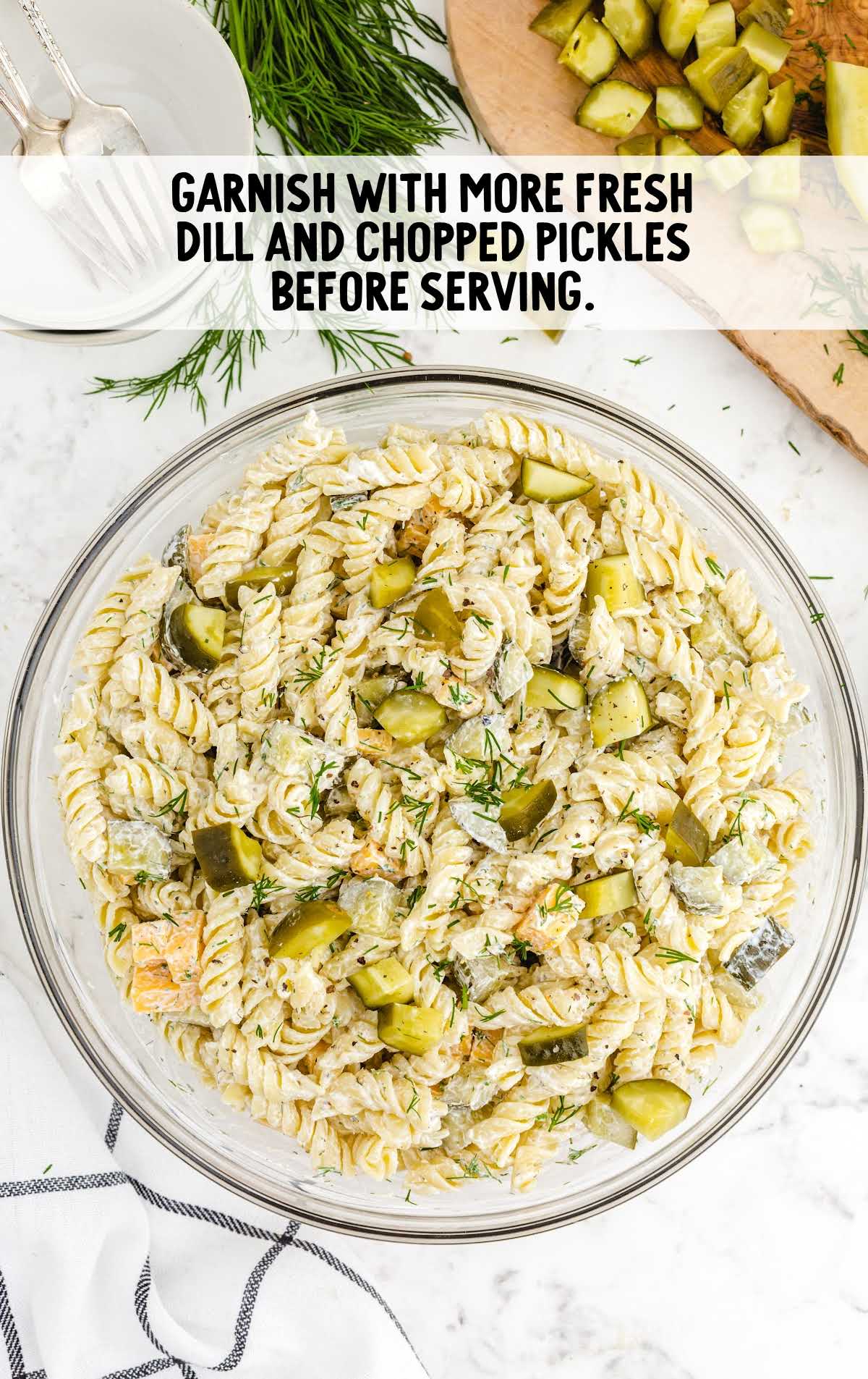 Top view of dill pickle pasta salad with text overlay that reads “Garnish with more fresh dill and chopped pickles before serving.”