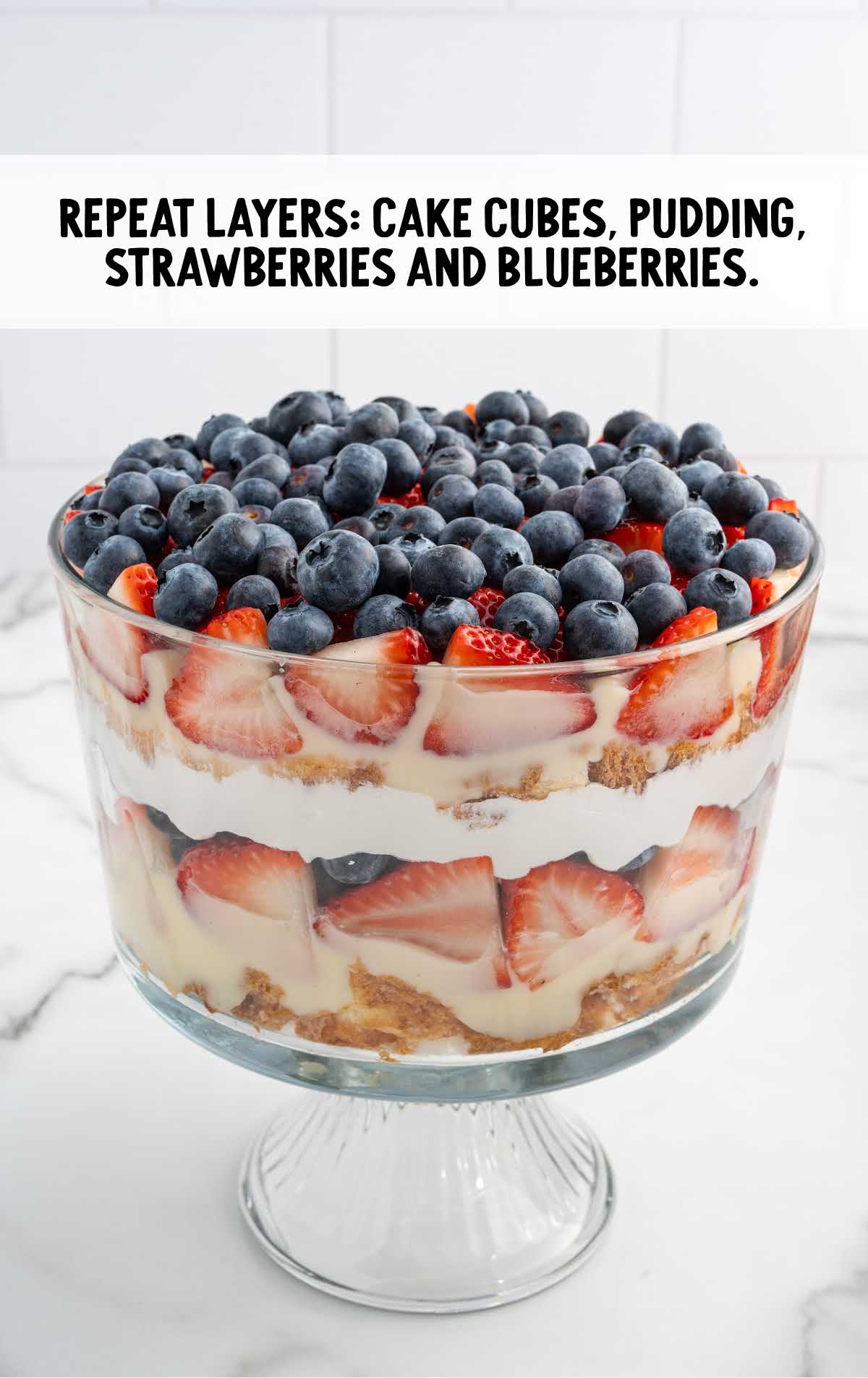 trifle layered with cake cubes, pudding, strawberries, and blueberries 