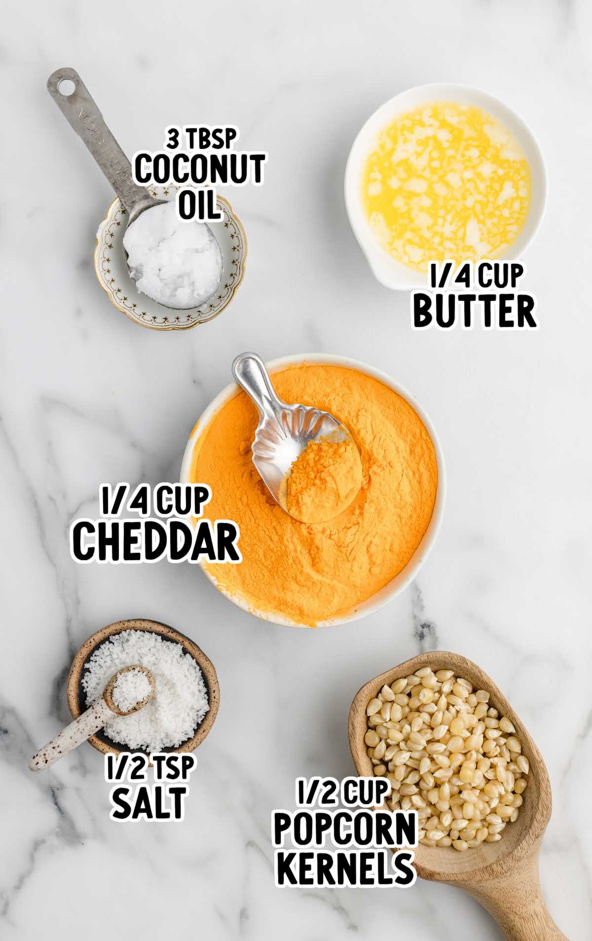 A flat lay of the ingredients for cheese popcorn, including popcorn kernels, cheese powder, coconut oil, butter, and salt, all labeled.