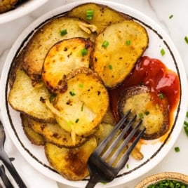 a bowl of fried potatoes topped with chives and served with ketchup