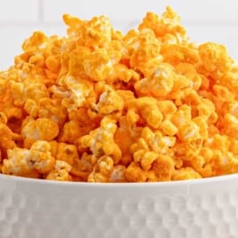 A large bowl of homemade cheese popcorn in a textured white bowl, with a golden cheddar cheese powder coating.