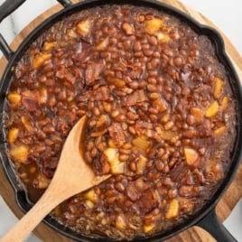 a skillet of Apple Pie Baked Beans with a wooden spoon