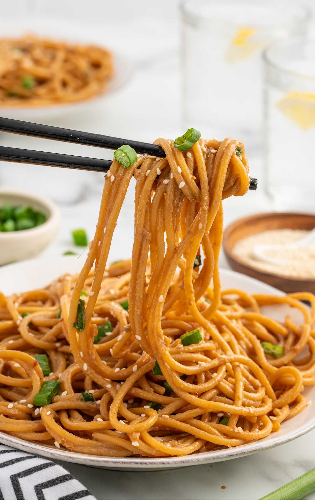 close up shot of Garlic Sesame Noodles on a plate being picked up by chop sticks
