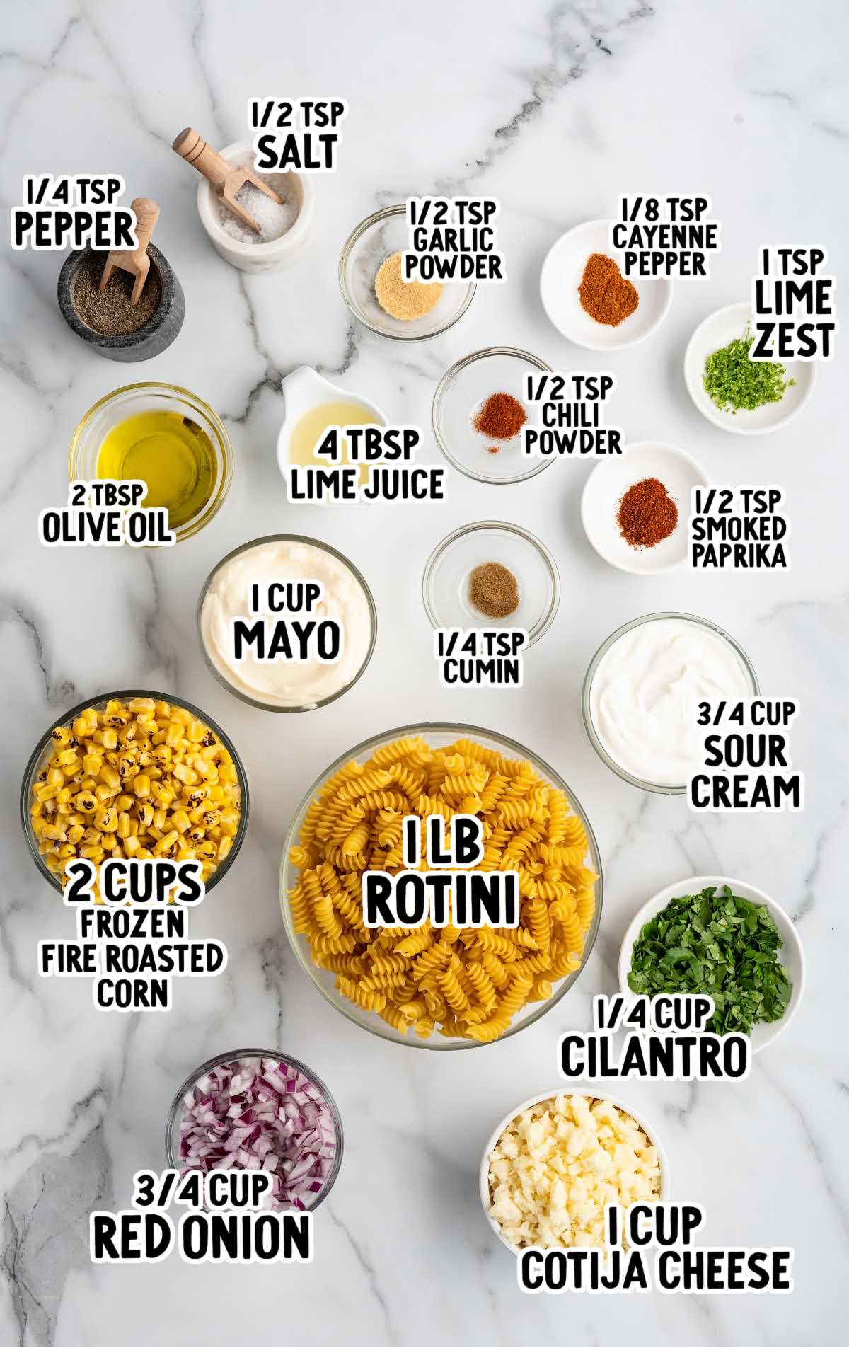 Labeled overhead layout of all ingredients for Mexican street corn pasta salad including rotini, corn, mayo, spices, cilantro, onion, and cheese.
