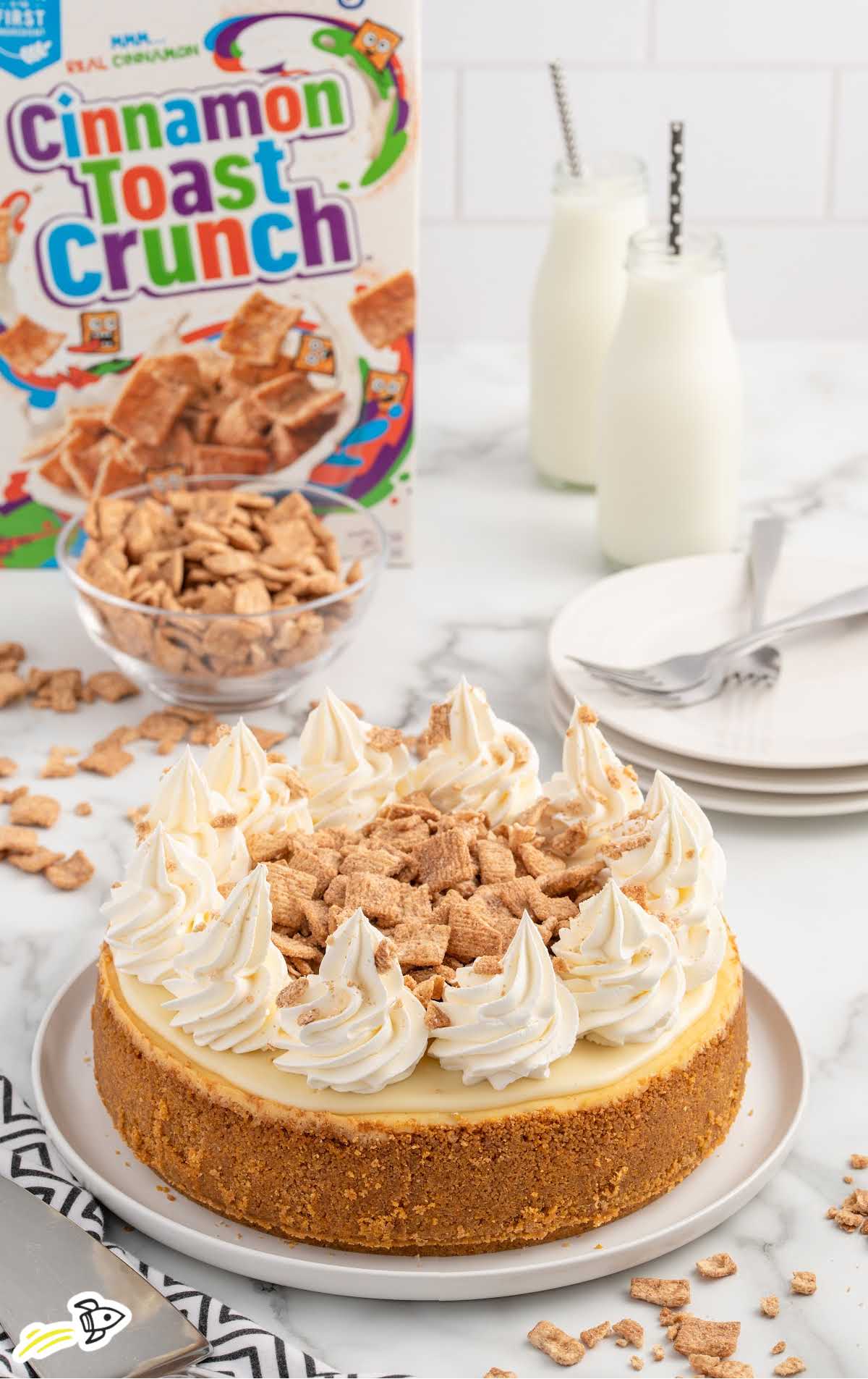 a Cinnamon Toast Crunch Cheesecake topped with whipped topping and cinnamon toast crunch cereal crumbs on a plate