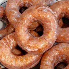 Plate filled with shiny homemade glazed donuts coated in sweet vanilla glaze.