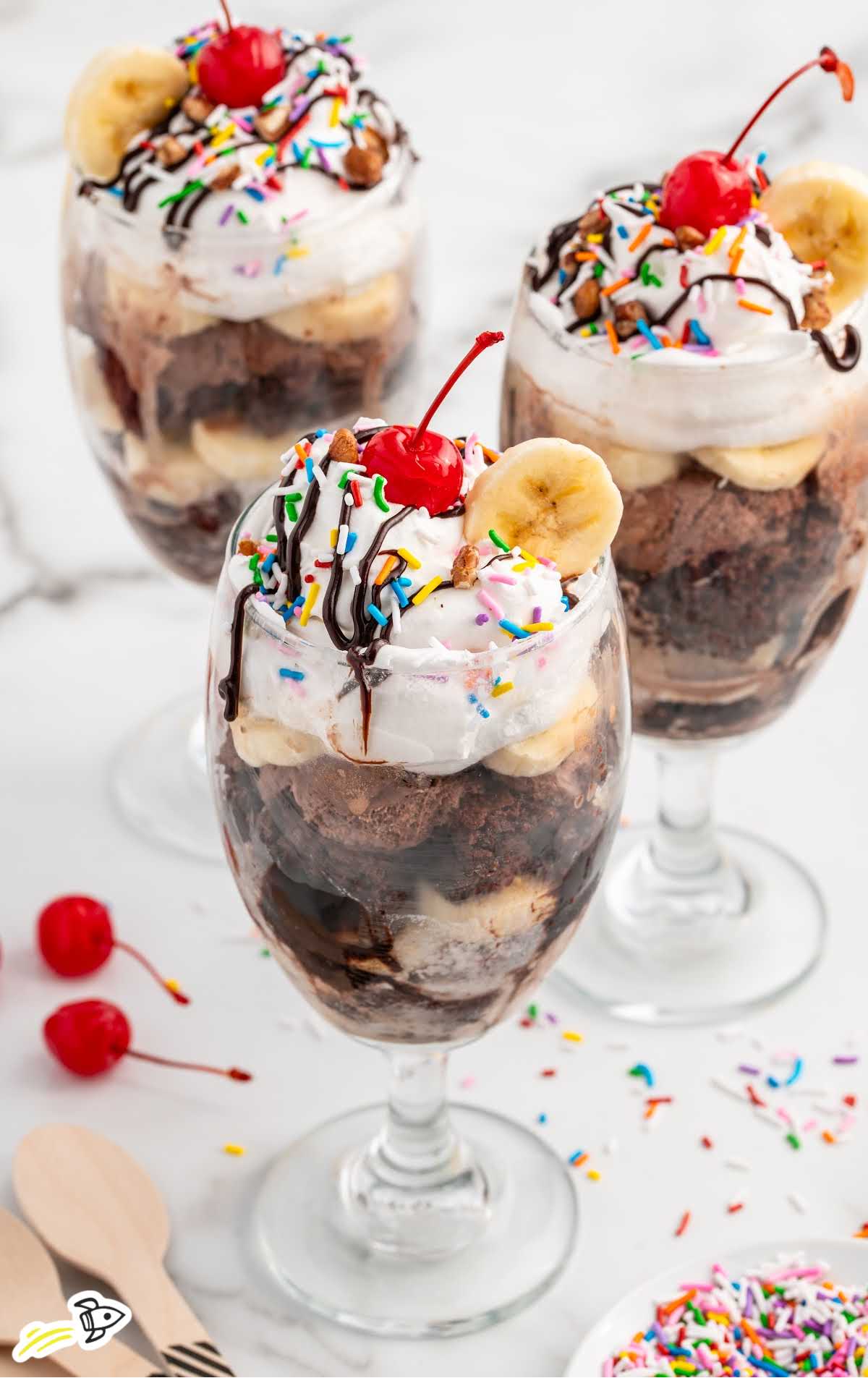 cups of Ice Cream Trifle topped with sprinkles, banana slices, cherries, whipped topping, and chocolate sauce