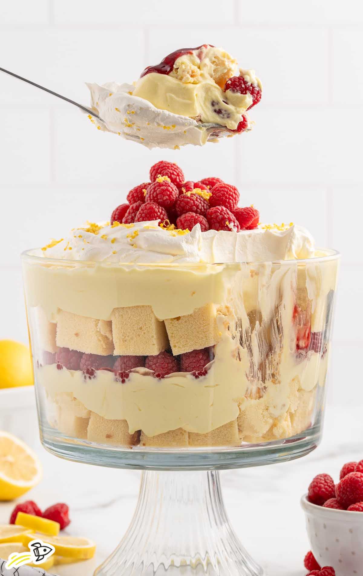 a trifle jar of Lemon Raspberry Trifle topped with raspberries and lemon zest with a spoonful of trifle scooped out