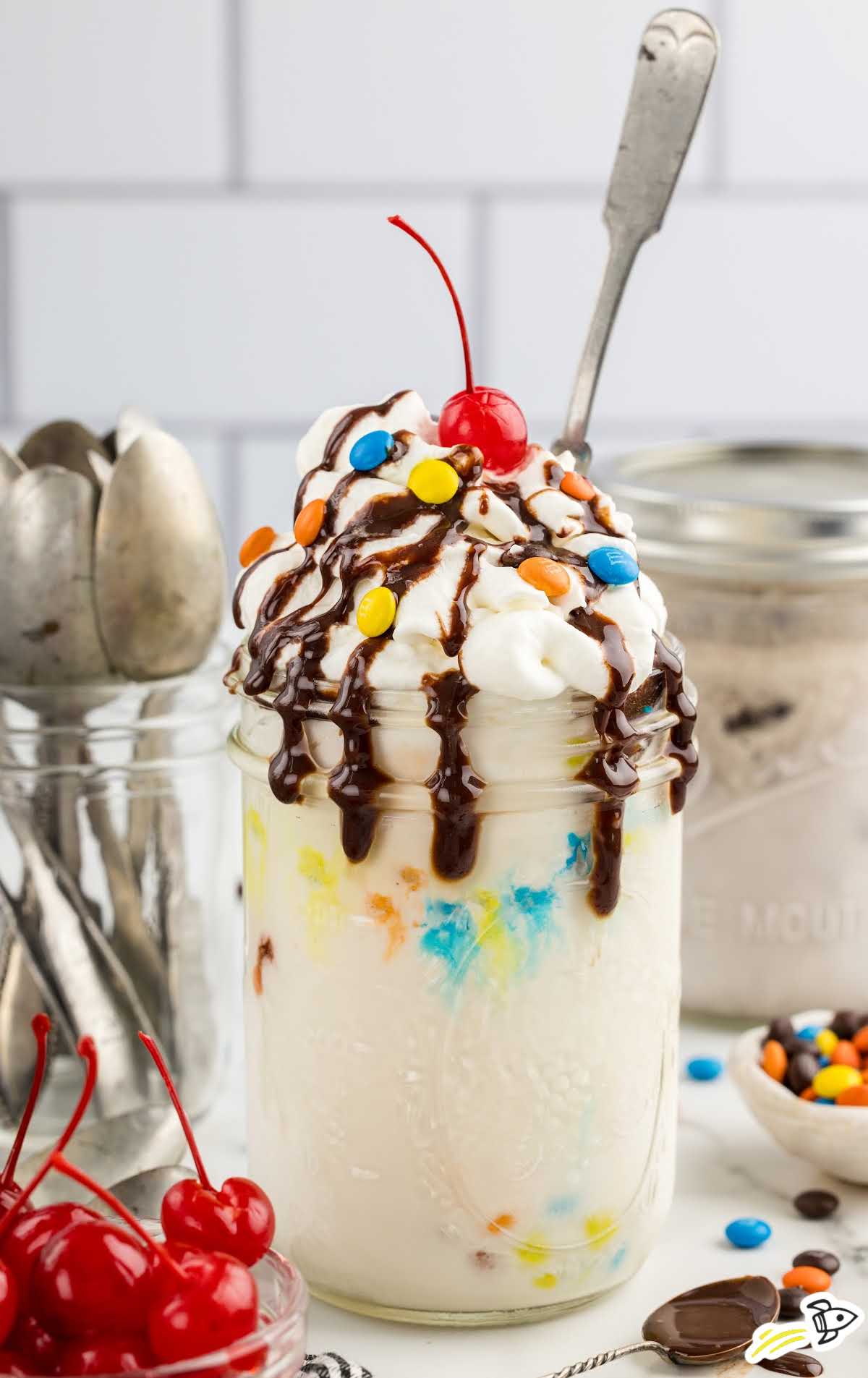 a Mason Jar of Ice Cream topped with chocolate syrup, m&ms, and a cherry