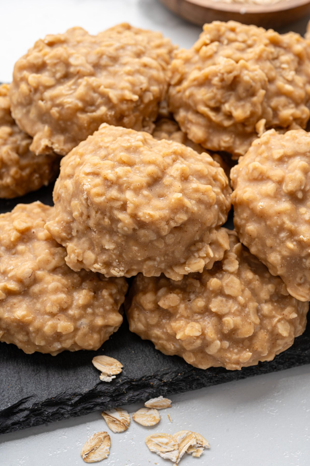 Close-up of no-bake peanut butter cookies stacked on a black slate board, showing their chewy, textured surface with visible oats."
