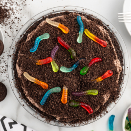 An overhead shot of a dirt pie beside a bowl of oreos and a bowl of gummy worms.