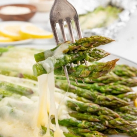 a plate of asparagus topped with melted mozzarella cheese