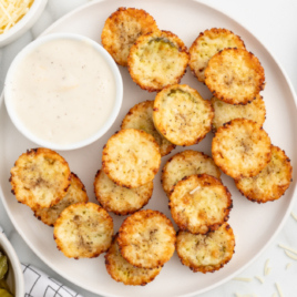 A white plate of pickle chips with sauce on the side.