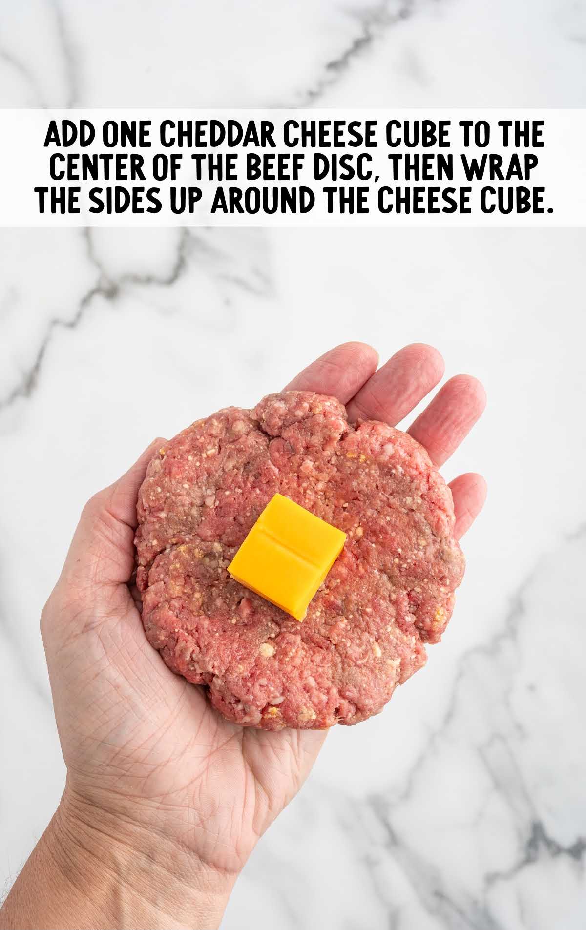 one cube of cheddar cheese placed into the center of the ground beef disc