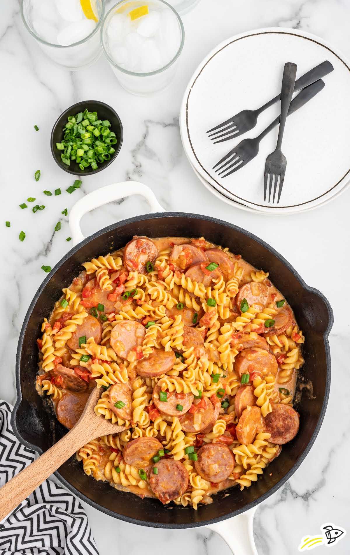 a skillet of Kielbasa pasta garnished with green onions