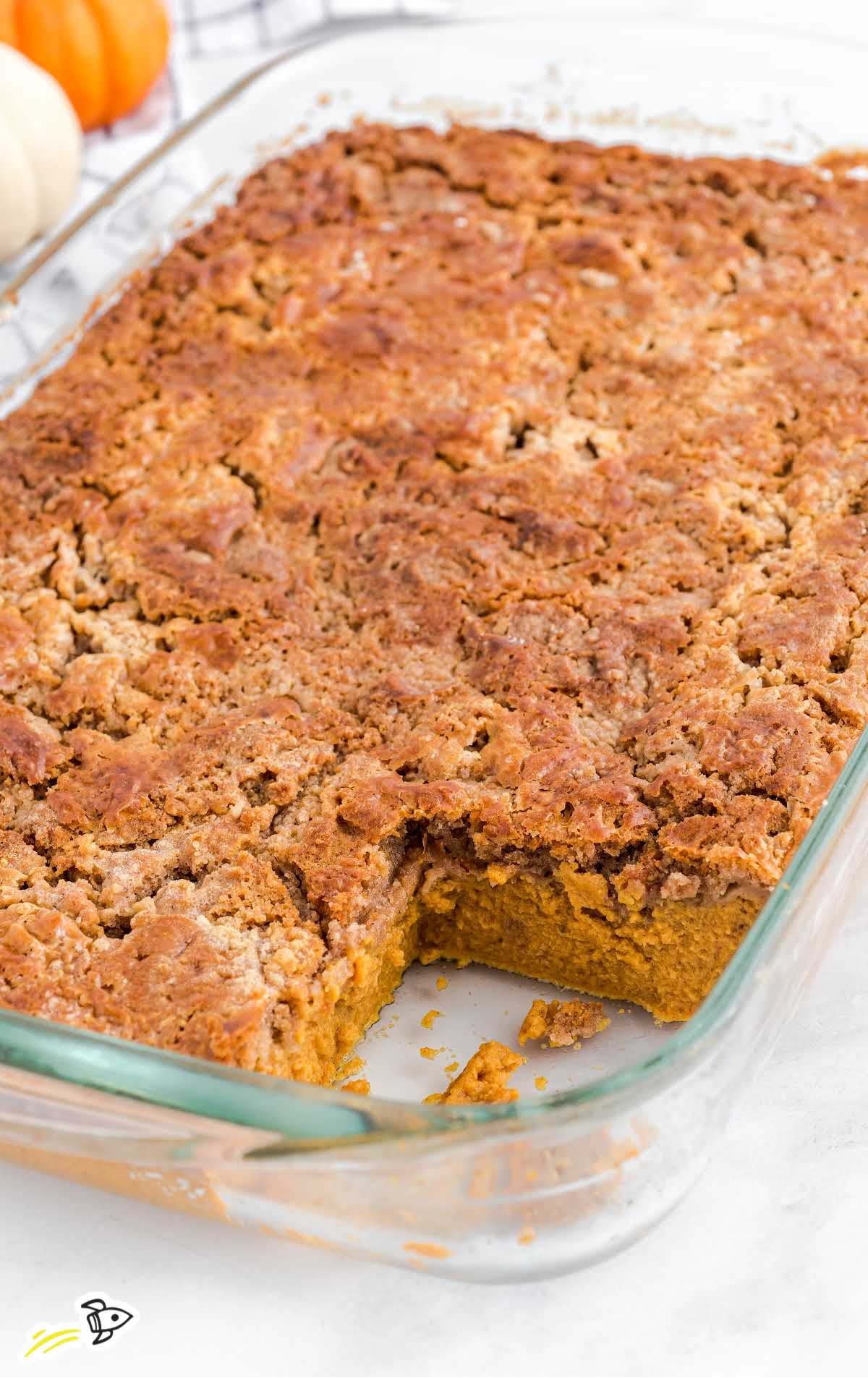 Glass baking dish filled with baked pumpkin dump cake with a corner piece removed.
