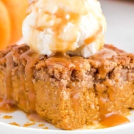 Slice of pumpkin dump cake topped with vanilla ice cream and caramel sauce on a white plate.