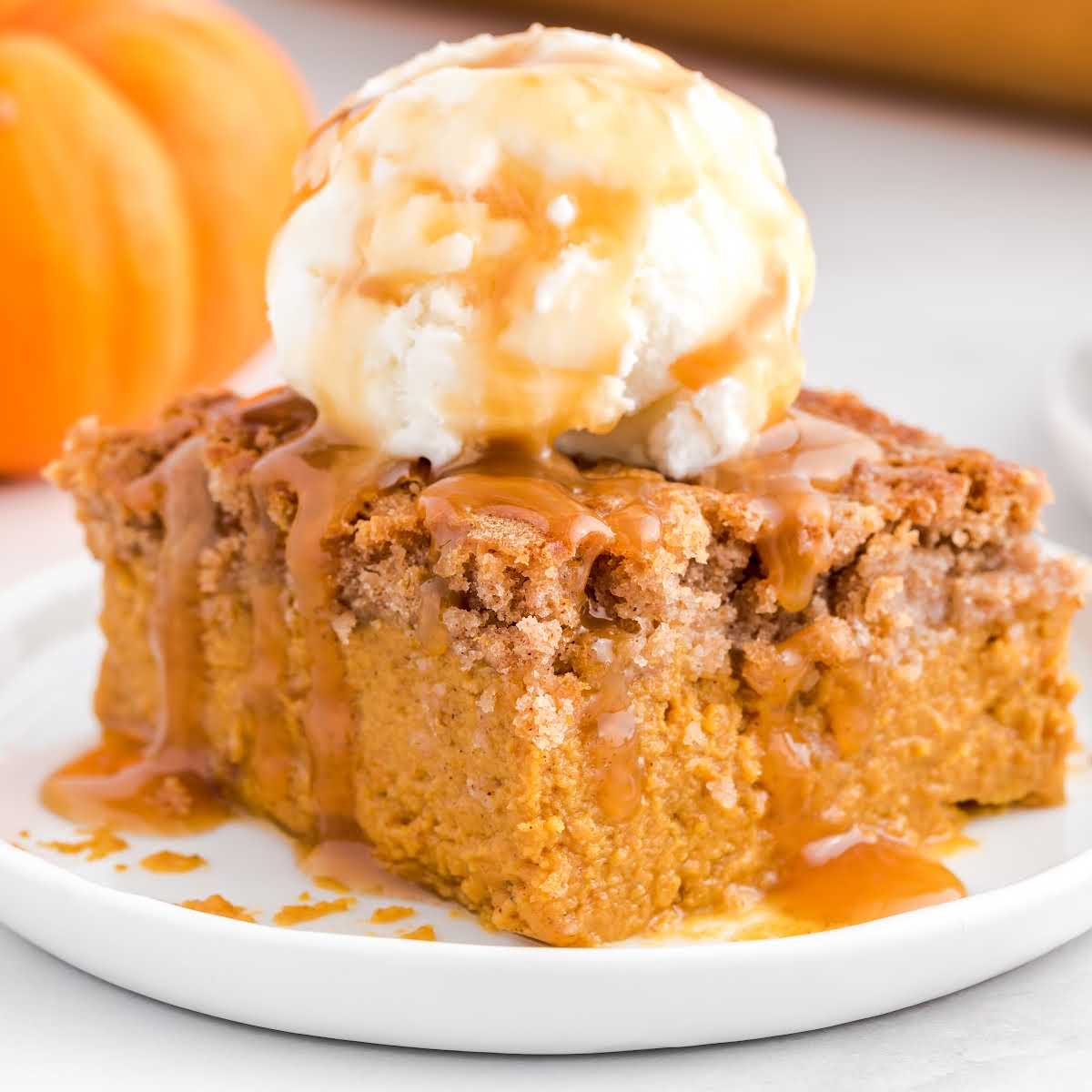 Pumpkin dump cake square topped with vanilla ice cream and caramel drizzle on a white plate.