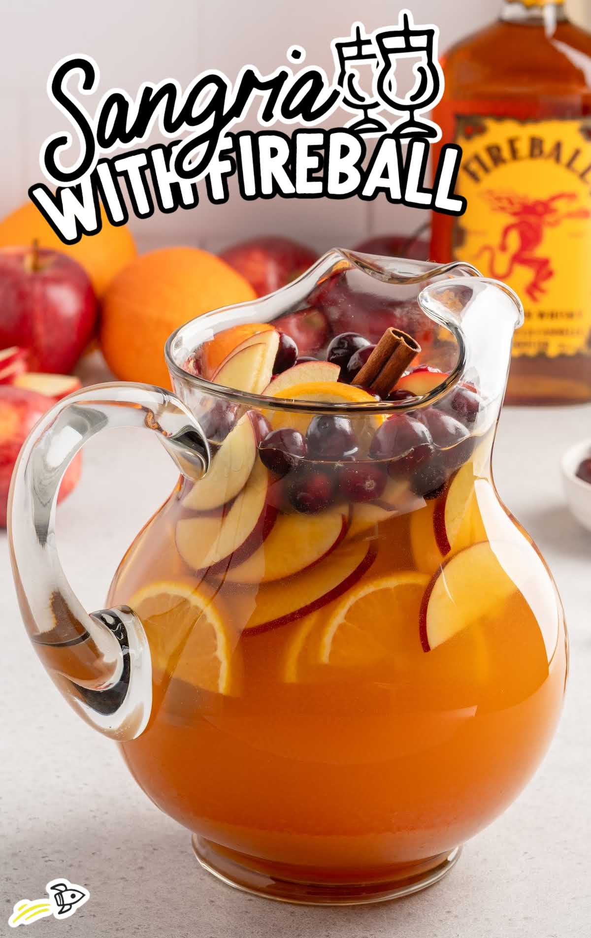 Large pitcher of apple cider sangria with Fireball whisky loaded with sliced apples, oranges, cranberries, and cinnamon sticks.