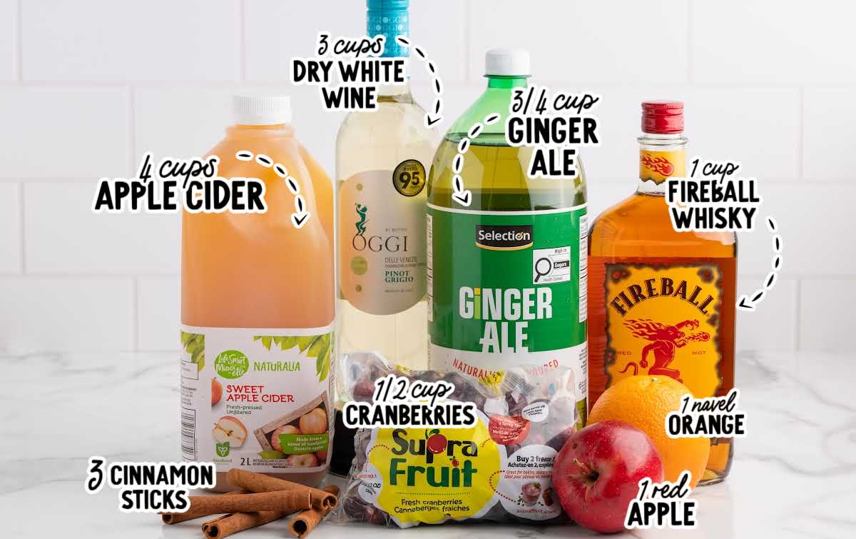 Ingredients for Fireball apple cider sangria including apple cider, white wine, ginger ale, Fireball whisky, orange, apple, cinnamon sticks, and cranberries.
