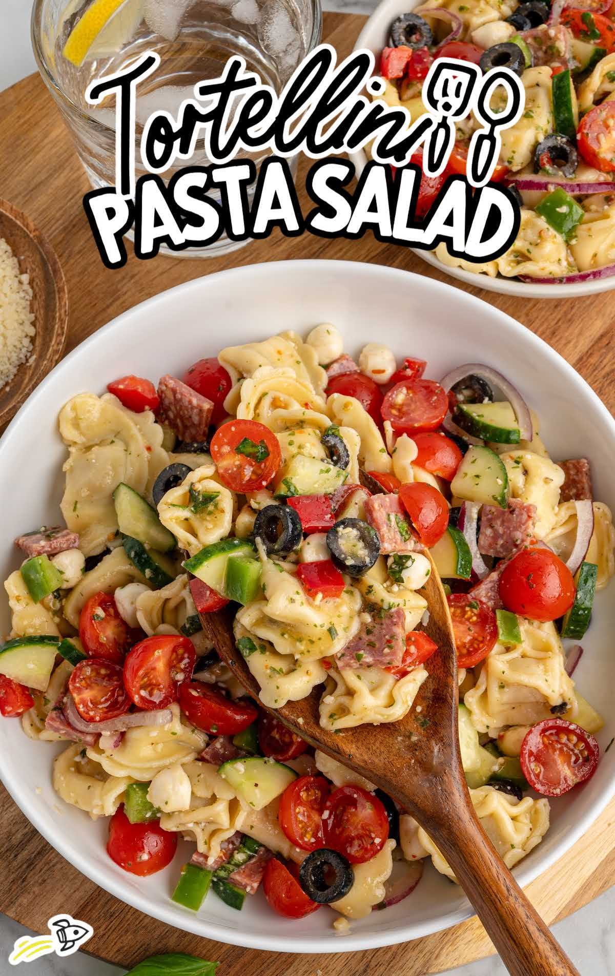 Bowl of tortellini pasta salad with cherry tomatoes, cucumbers, olives, mozzarella pearls, and salami mixed with zesty dressing.
