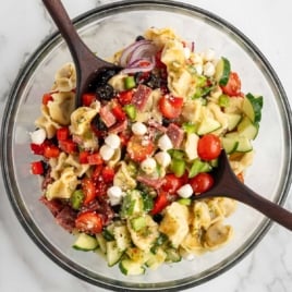 Overhead view of tortellini pasta salad in a glass bowl with vegetables, salami, mozzarella pearls, and Italian dressing.