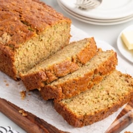 Zucchini bread loaf sliced on a wooden board with plates and forks in the background, perfect for recipe cards or social sharing.