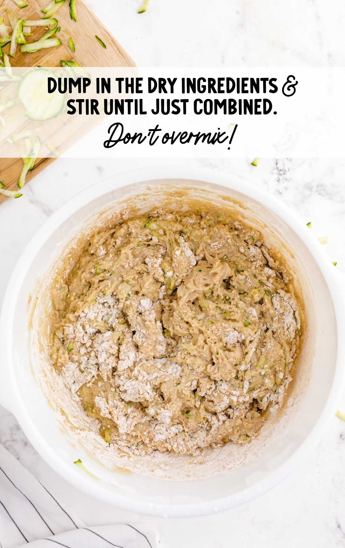 Zucchini bread batter being mixed in a bowl with dry ingredients partially combined, emphasizing not to overmix.