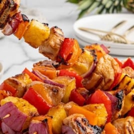 Close-up of grilled chicken pineapple kabobs on a white plate served with a bowl of rice