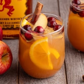 Close-up glass of Fireball apple cider sangria filled with oranges, apples, cranberries, and a cinnamon stick.