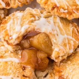 Close-up of a golden, flaky Air Fryer Hand Pie filled with gooey cinnamon apple filling, drizzled with white icing and sprinkled with coarse sugar. The pie is partially open, revealing the warm, spiced apple mixture inside.