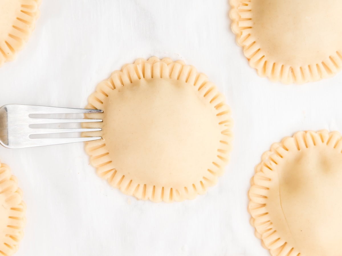 Uncooked round ravioli with crimped edges are arranged on a white surface, reminiscent of homemade Air Fryer Hand Pies. A fork is pressing the edges of one raviolo to seal it.