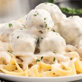 a plate of Alfredo Sauce with Meatballs served over pasta and garnished with parsley