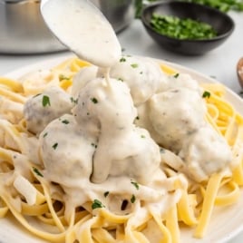 a plate of Alfredo Sauce with Meatballs served over pasta and garnished with parsley