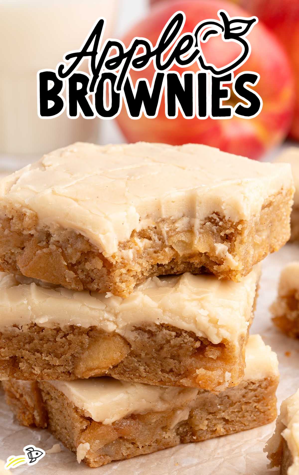 Stack of frosted apple brownies with a bite taken out, surrounded by more brownies