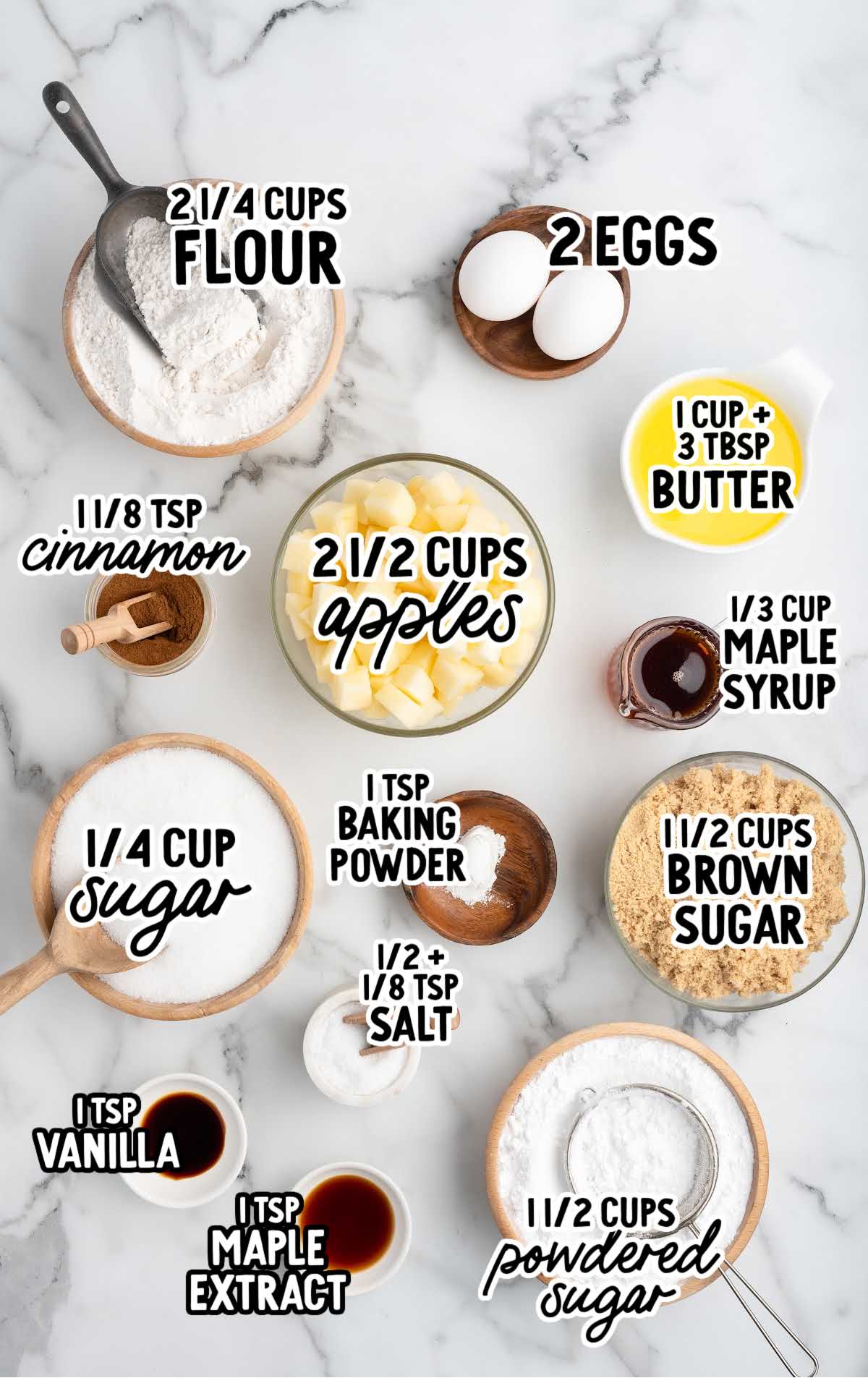 Flat lay of apple brownie ingredients including flour, eggs, butter, apples, cinnamon, sugars, and extracts with labeled text