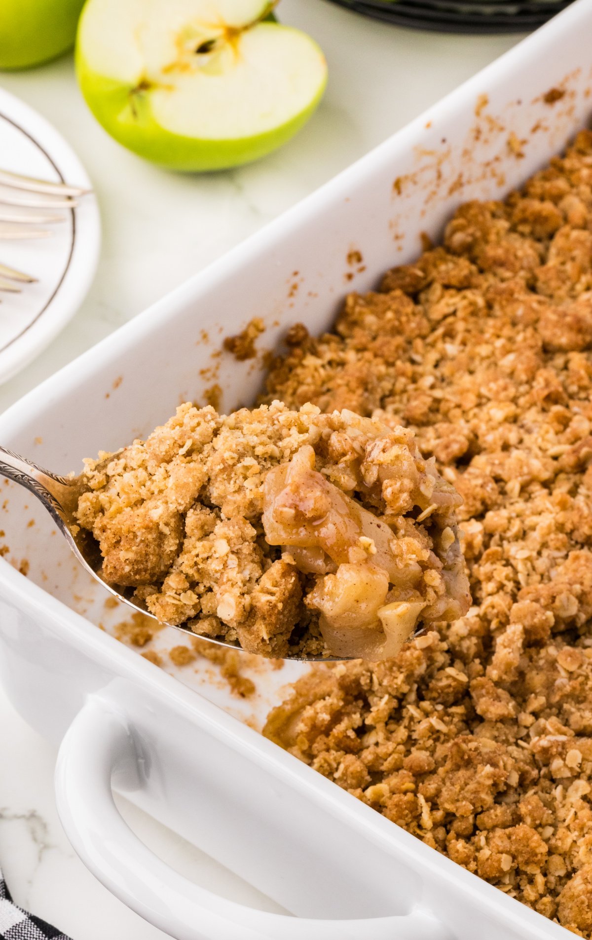 a baking dish of apple crisp with a serving spoon lifting out a scoop.