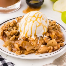 A dessert plate of apple crisp with ice cream and caramel sauce drizzle.