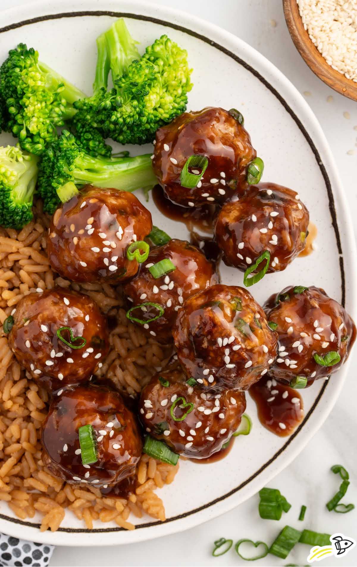 a plate of Asian Turkey Meatballs garnished with green onions and sesame seeds served with rice and broccoli