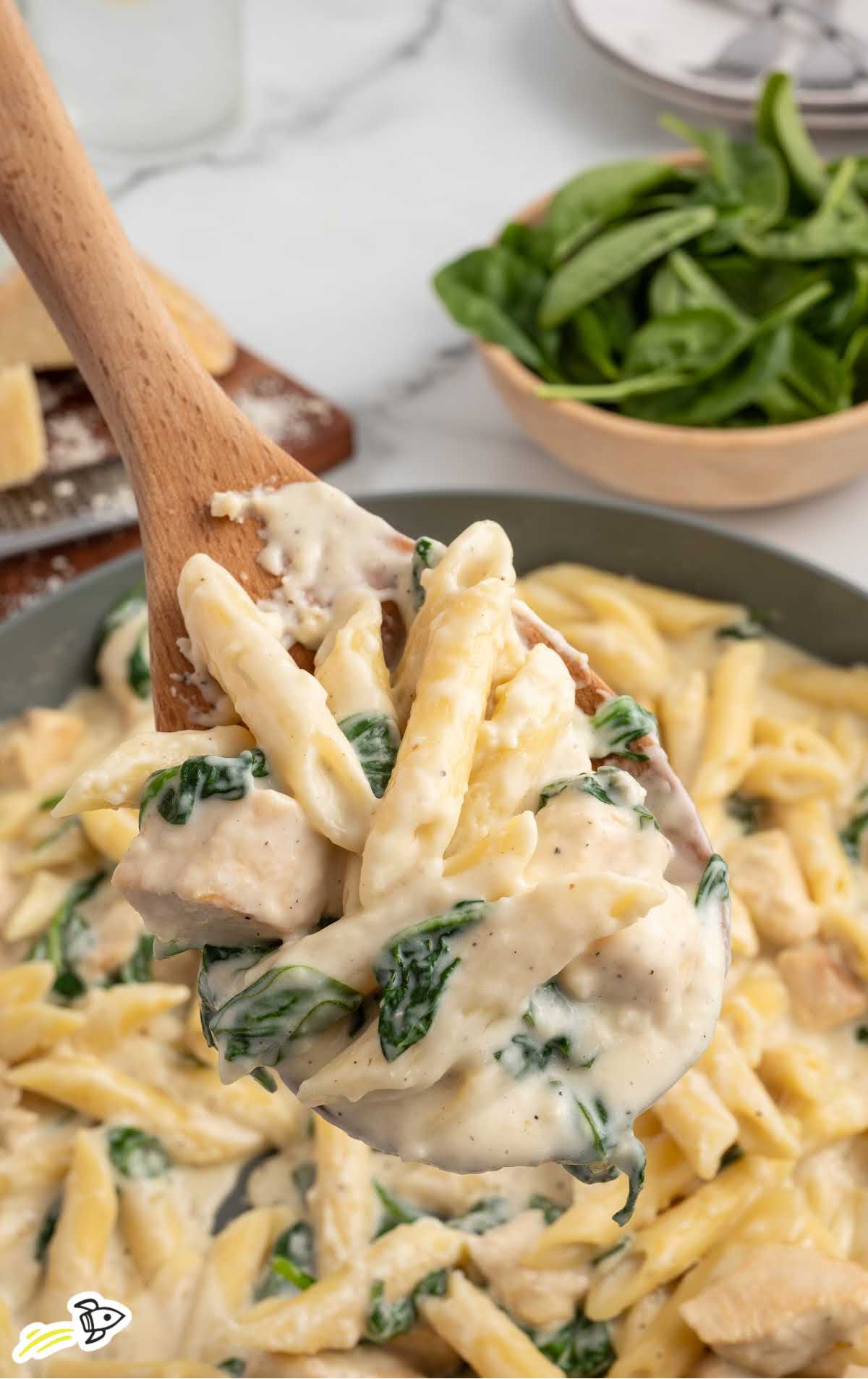 a pot of Chicken Spinach Alfredo with a large wooden spoon