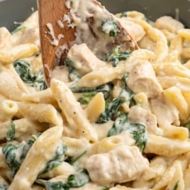 a pot of Chicken Spinach Alfredo with a large wooden spoon