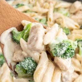 a skillet of Chicken and Broccoli Penne Alfredo with a large wooden spoon