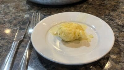 A small dumpling coated in savory broth, reminiscent of a classic Chicken and Dumplings Recipe, sits on a white plate next to a fork and knife on a granite countertop.